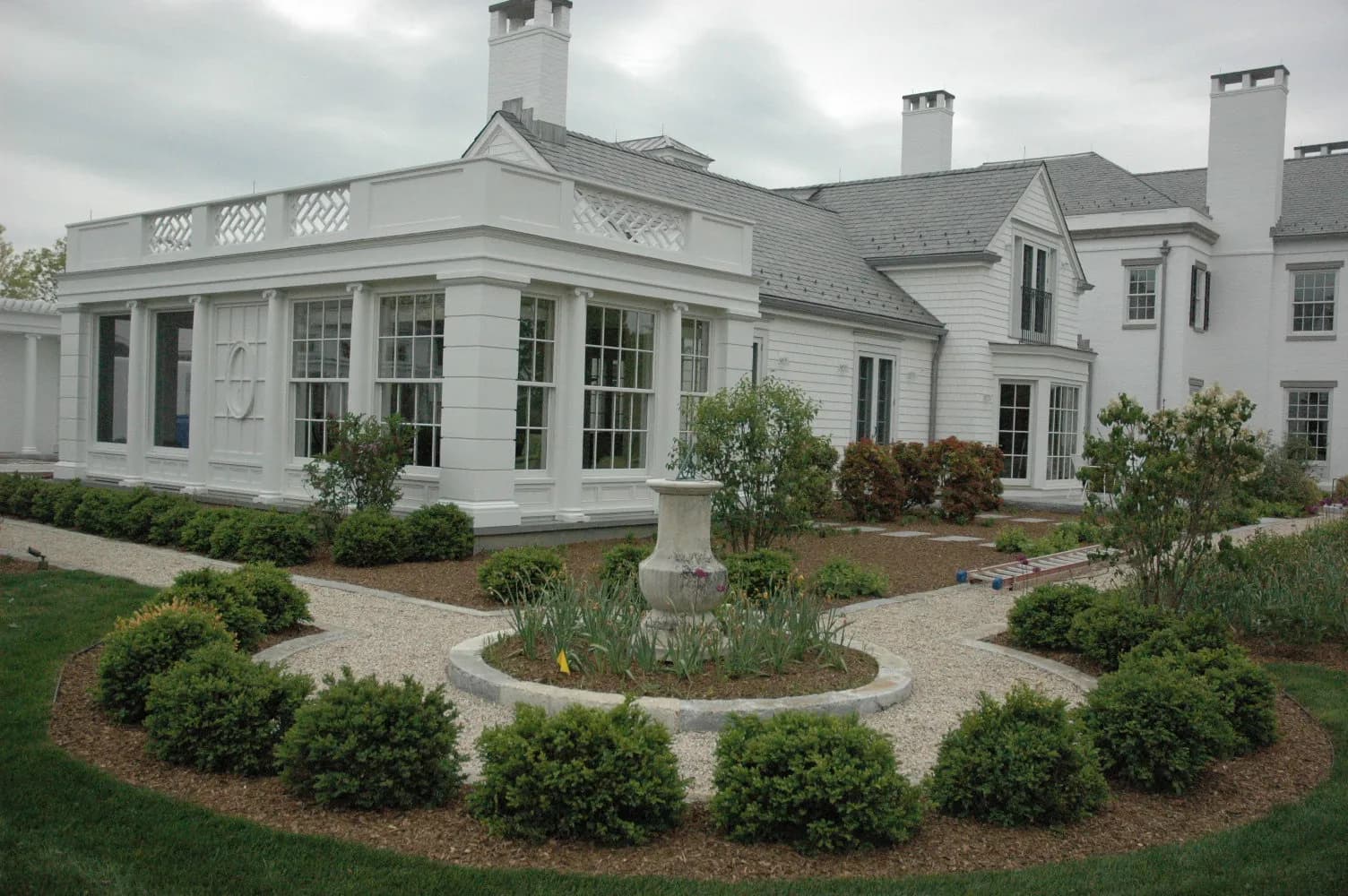 Elegant white house with large windows, manicured garden, and paths made of gravel and plants.