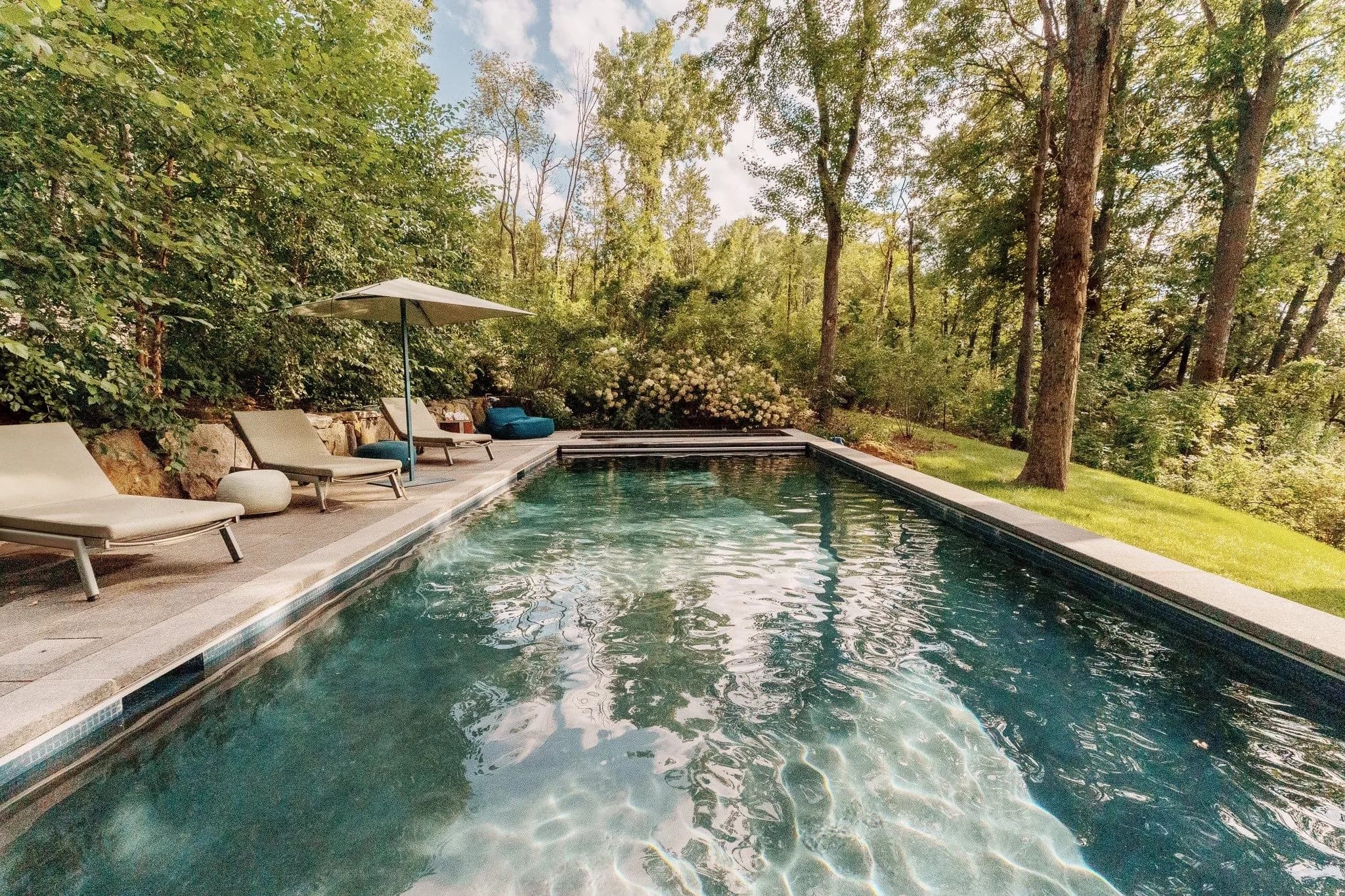 Modern backyard swimming pool surrounded by lush greenery and outdoor seating.
