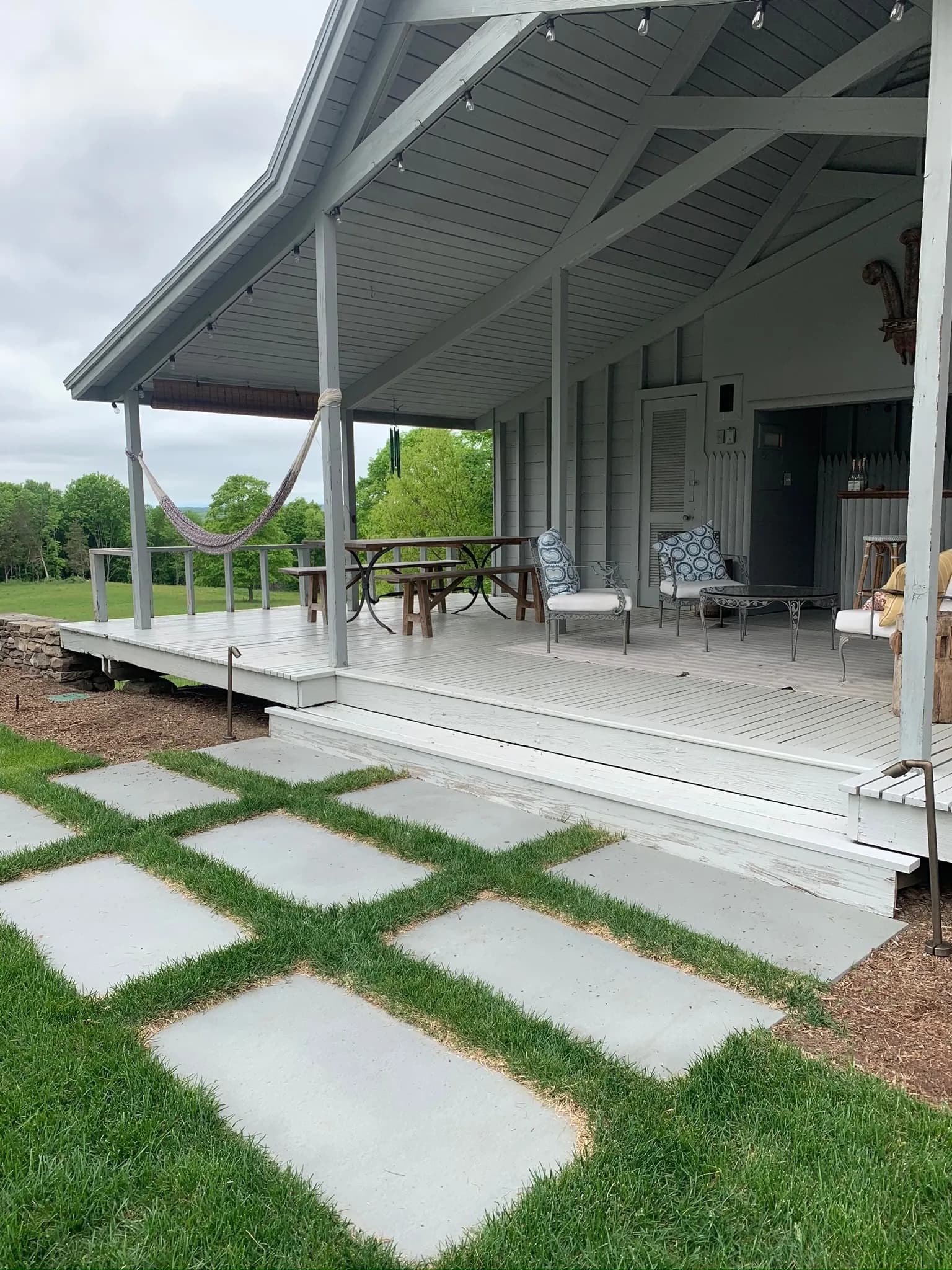 Charming porch with seating and pathway, surrounded by lush greenery and cloudy skies.