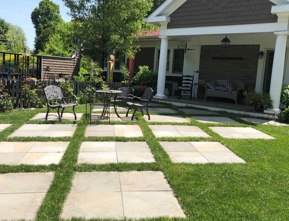 Outdoor patio with stone pavers, green grass, and a table with chairs near a house.