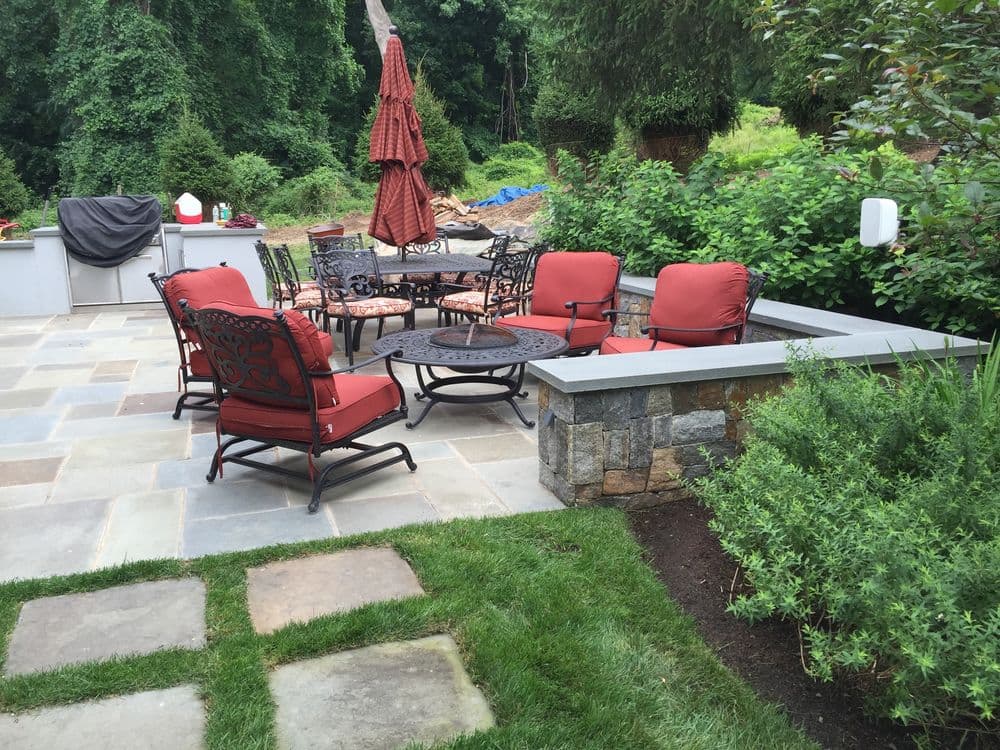 Outdoor patio with red cushioned chairs and table, surrounded by lush greenery.