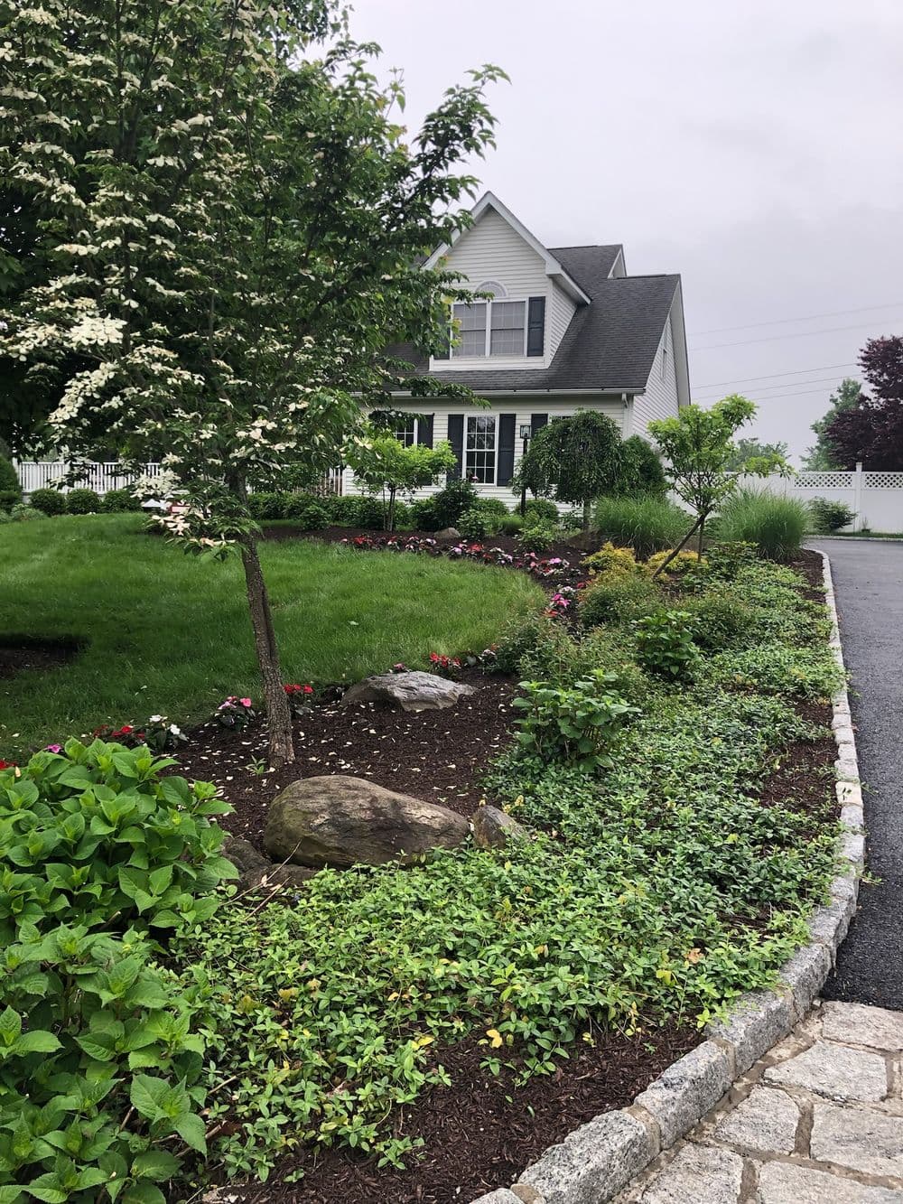 Charming house with landscaped garden, colorful flowers, and stone pathway on a cloudy day.