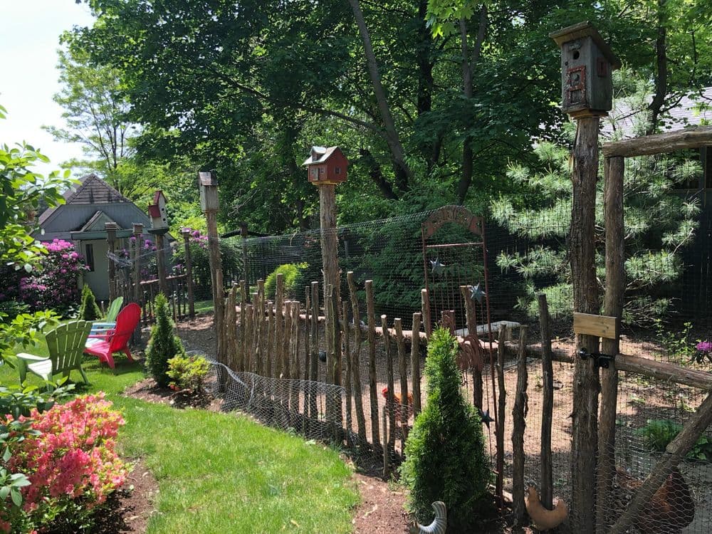 Birdhouses along a rustic fence in a garden, featuring vibrant flowers and greenery.