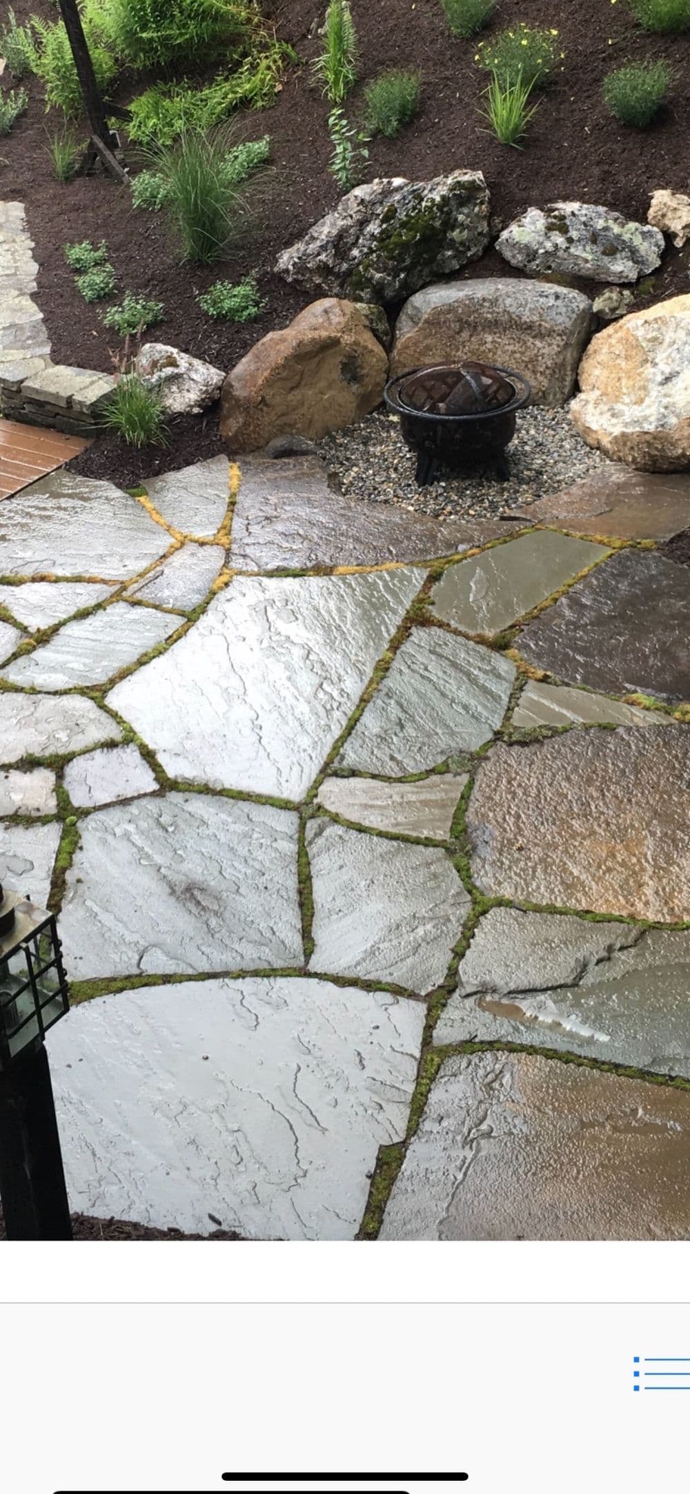 Rain-soaked stone patio with natural stone borders and lush green landscaping.