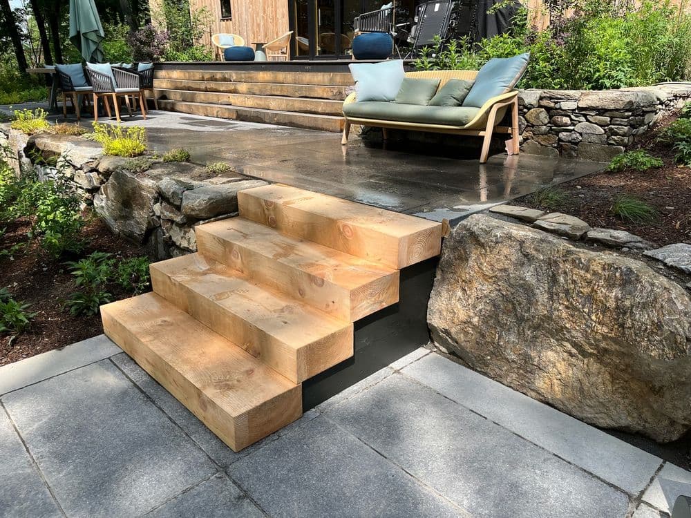 Wooden staircase leading to a patio area with stone landscaping and outdoor seating.
