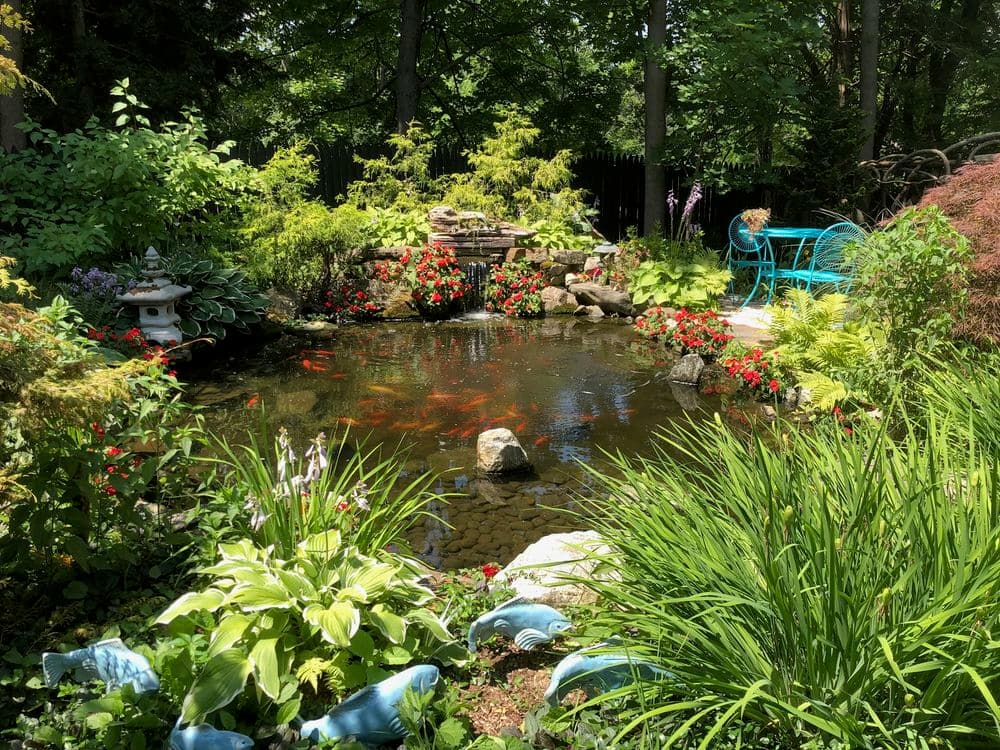 Lush garden with a koi pond, colorful flowers, and a teal seating area surrounded by greenery.