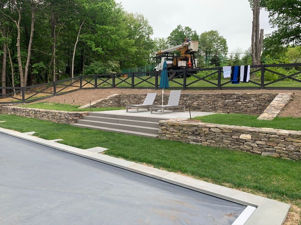 Backyard landscaping with stone steps, lounge chairs, and towels hanging on a fence.